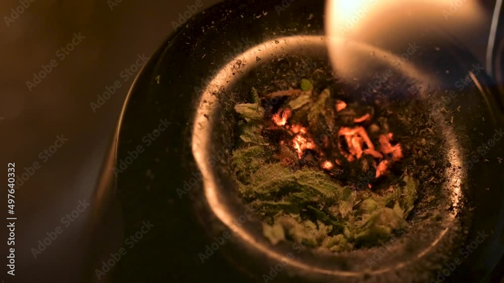 Macro view of lighting marijuana and smoking through a large water pipe.  Burning cannabis releasing THC and CBD.  Recreational drug use concept.