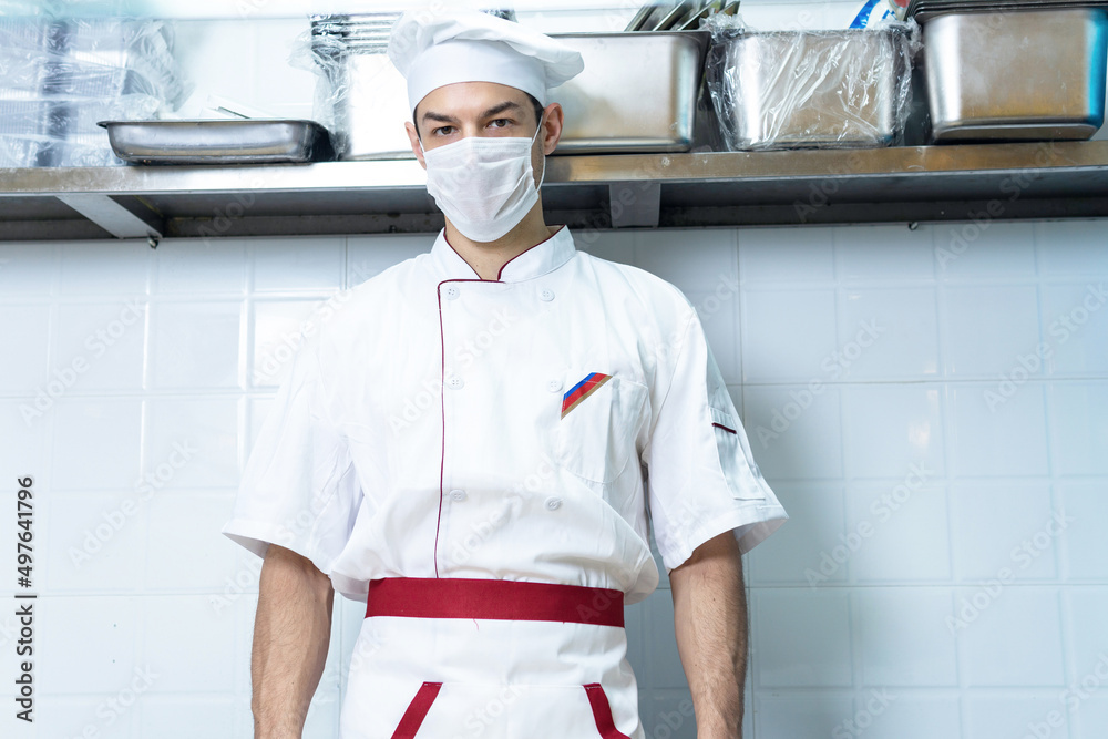 Male chef cook wearing face protective medical mask for protection from virus disease at restaurant kitchen. Health, safety and pandemic concept