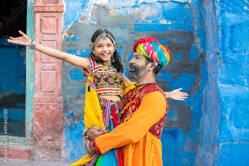 Portrait of happy indian father holding daughter with open arms pose wearing traditional colorful rajasthani outfit. rural india family. copy space, smiling girl with her dad playing. photo