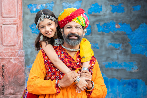 Portrait of happy indian father daughter hugging wearing traditional colorful rajasthani outfit looking at camera. rural india family. copy space photo