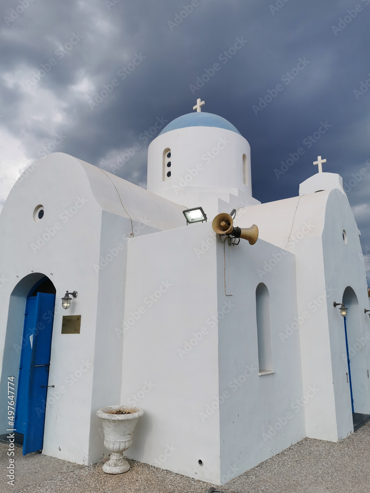 The Church of St. Nicholas the Wonderworker is white with a blue door against the backdrop of the dramatic sky. The Church of St. Nicholas the Wonderworker is white with a blue door against the backdrop of the dramatic sky.