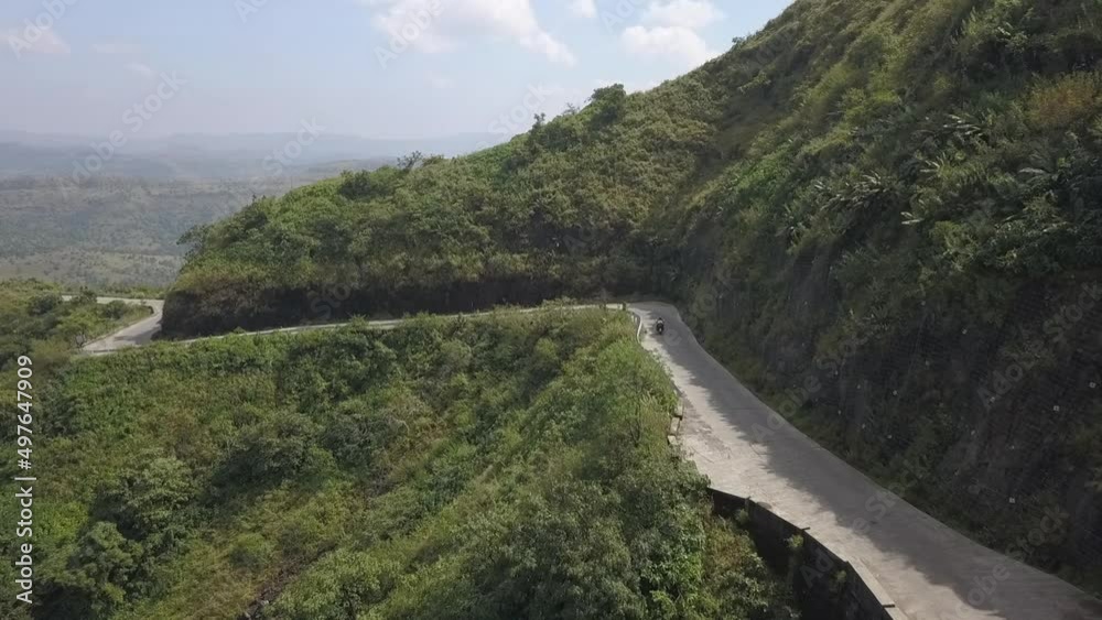 Aerial follows motorcycle on twisty road cut into steep mountain side Aerial follows motorcycle on twisty road cut into steep mountain side
