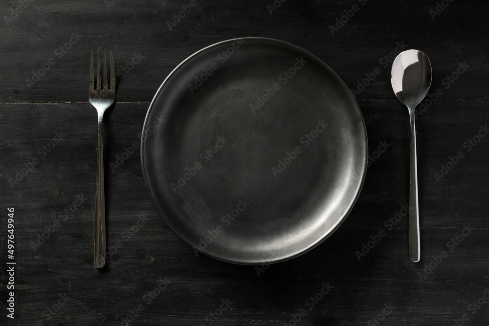 Modern black dining table setting with empty black plate, fork and spoon. Modern black dining table setting with empty black plate, fork and spoon.
