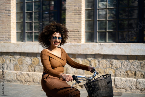 Smiling black woman riding bicycle along building photo