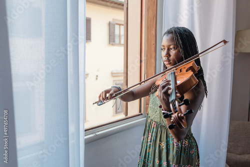 Black girl by a window playing viola