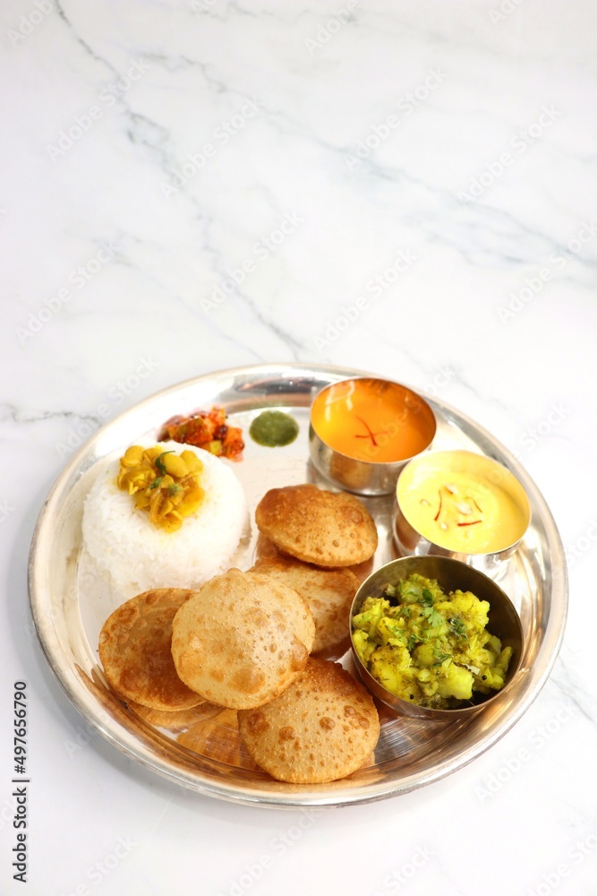 Indian vegetarian Thali or platter includes Aloo ki sabji, dal rice, Puri bhaji, Shrikhand or Srikhand, Aamras, papad, pickle, and chutney. Indian food is served in a Silverplate or thali. Copy Space.