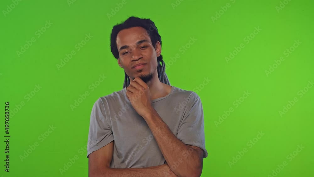 Young confident serious African American man thinks and touches chin thinking about future life plans and goals dressed in simple beige t-shirt on chroma key background. People, thoughts, lifestyle. Young confident serious African American man thinks and touches chin thinking about future life plans and goals dressed in simple beige t-shirt on chroma key background. People, thoughts, lifestyle.