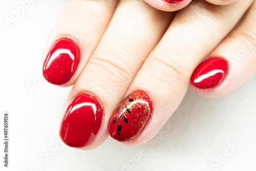 Female hands closeup with red nails. Delicate black painting, small decor with golden foil, bright gel polish. Selective focus on the details, blurred background.