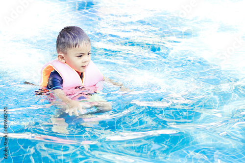 Cute boy wearing safety inflatable armbands swimming in swimming pool