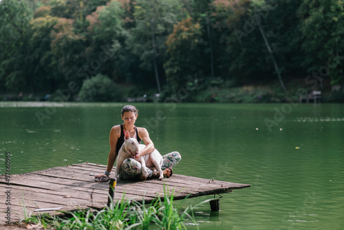 Woman relaxing at a lake with a bullterrier dog photo