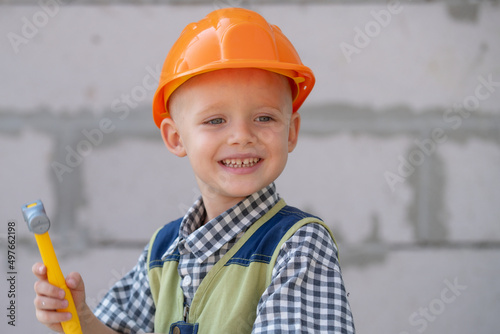 Kid in hard hat holding hammer. Happy smiling little child helping with toy tools on construciton site. Kids with construction tools. Construction worker.