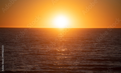 Sunset with large yellow sun under the sea surface. Calm ocean with sunset sky and sun through the clouds over. Calm ocean and sky background.
