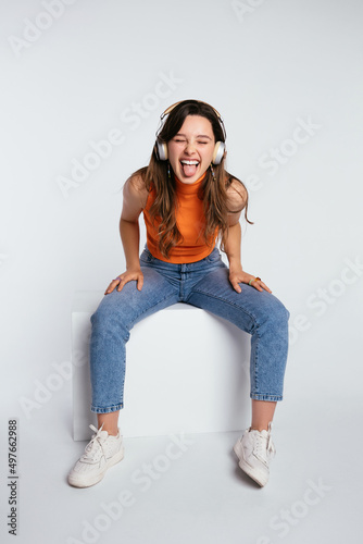 Joyful teenage lady in headphones showing tongue