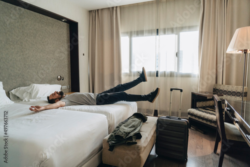 Relaxed man jumping on bed in hotel room