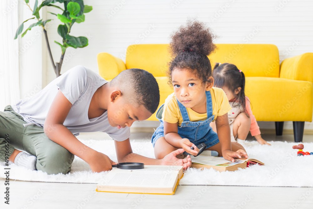 Little kid girl and boy reading book with magnifier on the floor, Happy children playing in the living room Little kid girl and boy reading book with magnifier on the floor, Happy children playing in the living room