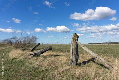 A broken barbed wire fence with old rustic wooden posts against a blue sky background