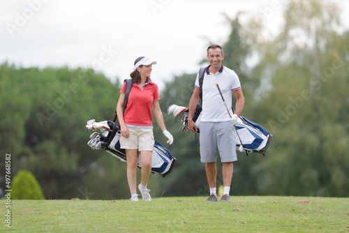 middle aged couple carrying golf bags on the green