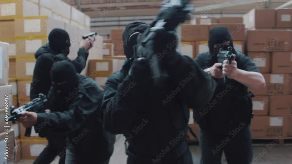 A special forces military team raid a warehouse with guns drawn wearing balaclavas an gas masks