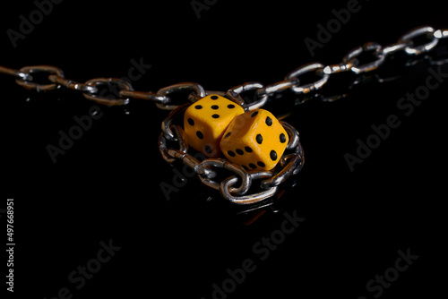 Gambling addiction. Two dice wrapped in a chain on a black background 