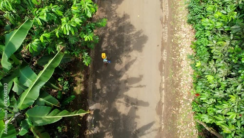 Aerial view above a woman carrying canister on head, walking on a road in Sao Tome, Africa - top down, drone shot photo