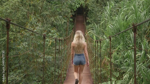 Active blond woman hiking on jungle suspension bridge going on adventure photo