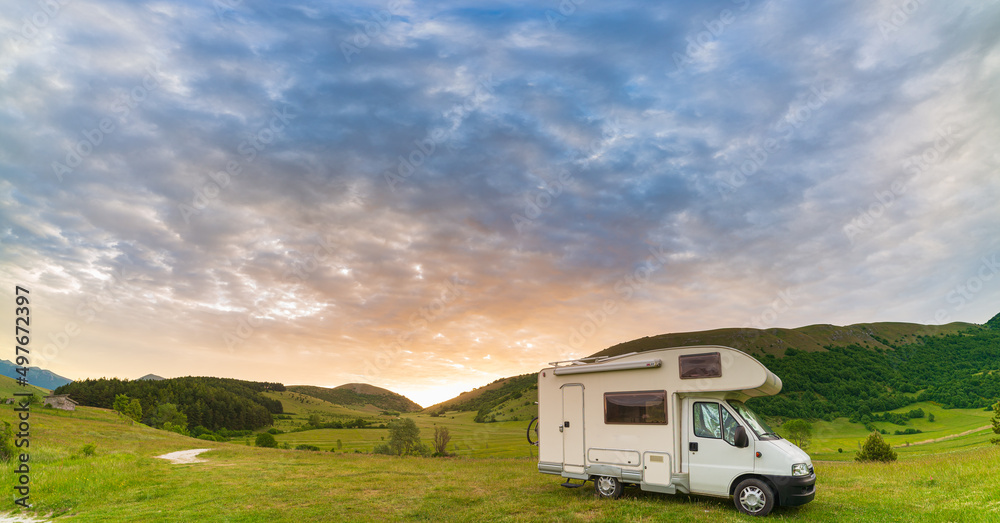 Sunset dramatic sky over camper van in Montelago highlands, Marche, Italy. Epic clouds above unique hills and mountains landscape, alternative vanlife vacation concept.