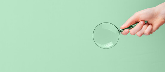 Banner with hand holding magnifying glass. Information search, key words finding, data analysis and verification concept. Copy space on green background in eco-friendly style. High quality photo