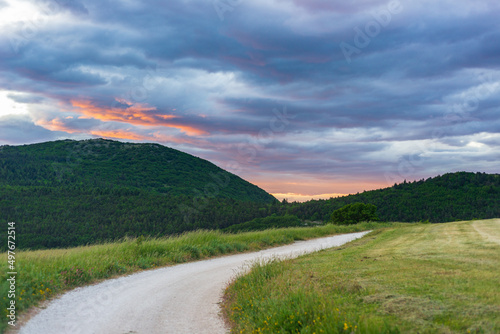 Sunset dramatic sky over country road in Marche region, Italy. Epic clouds above winding trail unique hills and mountains landscape, emotional feeling concept.