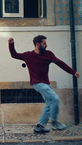 Vertical Screen: Cheerful Young Adult Man in Casual Clothes Actively Dancing while Walking on the Street of an Old Town in a City. Scene Shot in an Urban Environment on an Quiet Small Town Street. photo