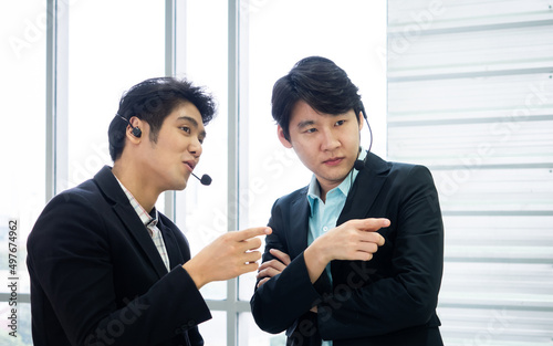 Asian two businessman talk and discuss support plan together while pointing finger in the same time at call center office