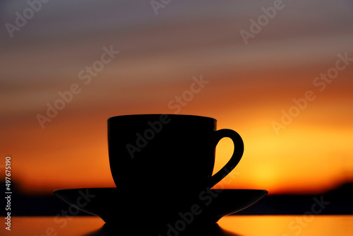 Black silhouette of coffee or tea cup on sunset background. View from the window to orange sky