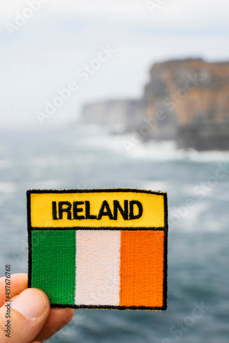 Sign Ireland and Irish flag in focus. D  n Aonghasa and cliffs of Inishmore  Aran islands  Irelandin the background. Popular tourist landmark with stunning Irish nature scenery. Blue ocean and sky.