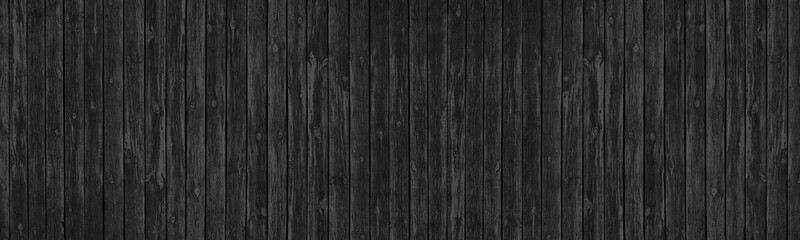 Old black knotted wooden board wide panoramic texture. Dark gray rough wood plank long backdrop. Large abstract background