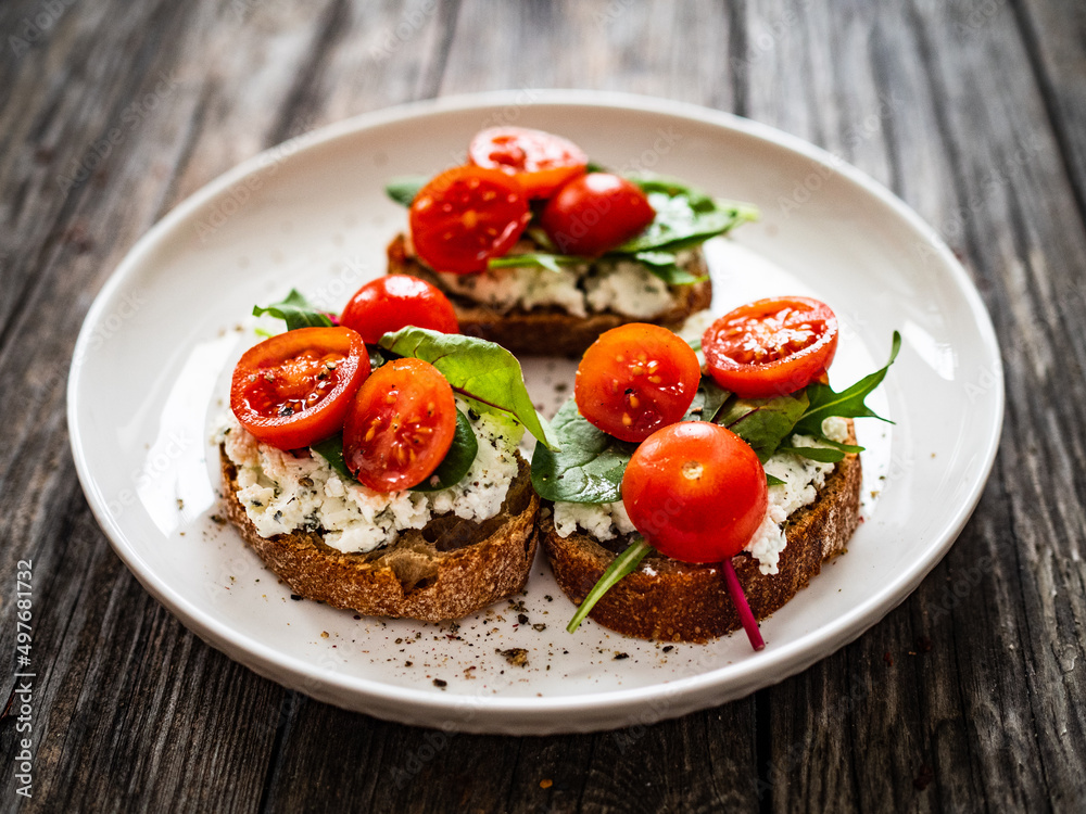 Tasty sandwiches - toasted bread with cream cheese, cherry tomatoes and green leaves on wooden table
Tasty sandwiches - toasted bread with cream cheese, cherry tomatoes and green leaves on wooden table