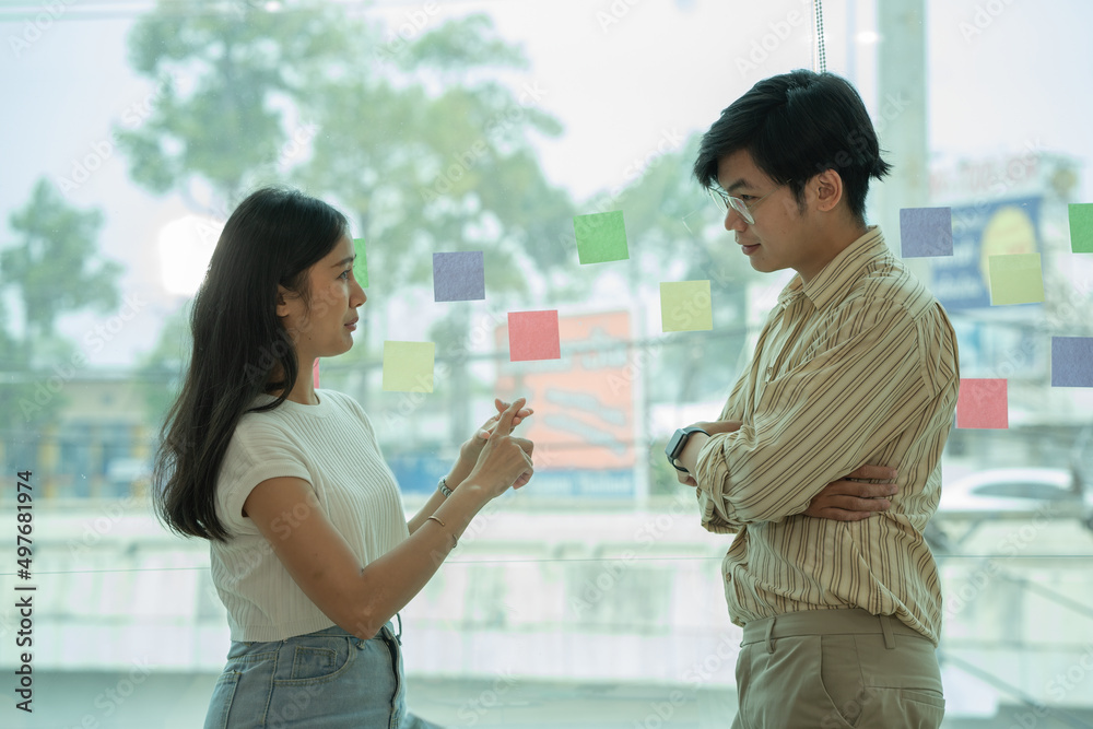 Asian business colleagues standing and talking by the office window Asian business colleagues standing and talking by the office window