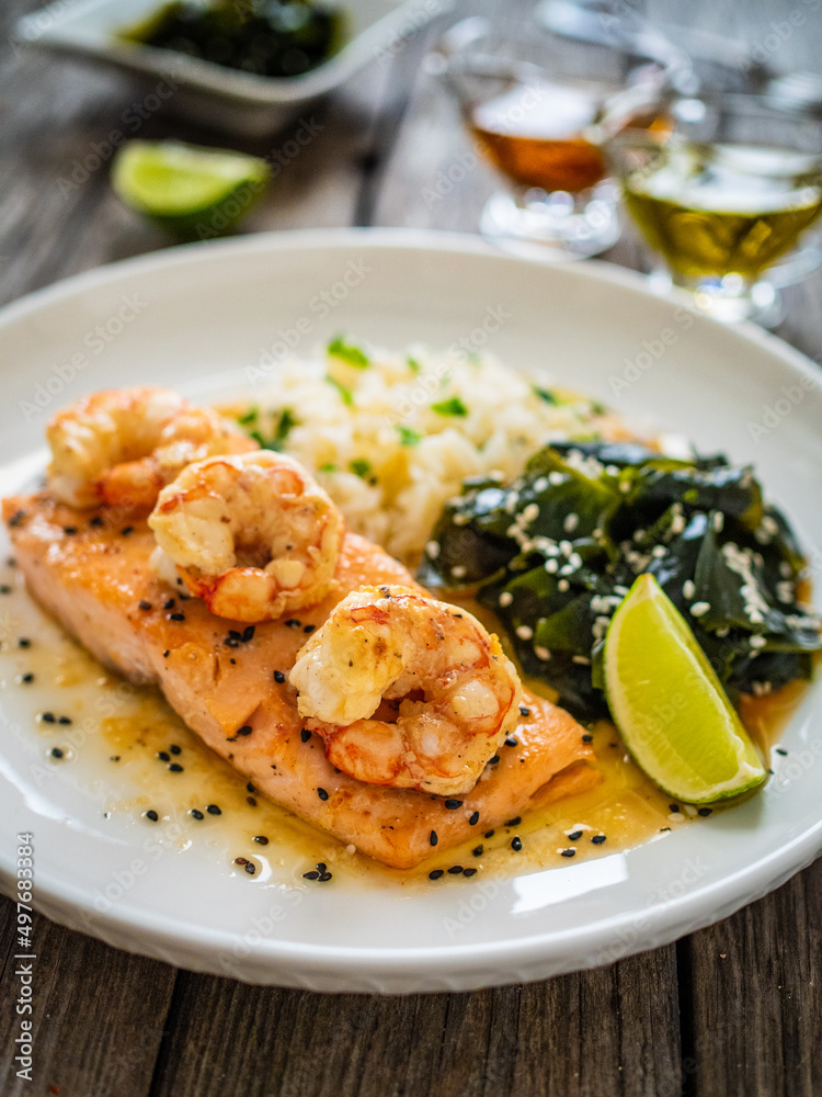 Fried salmon steak with prawns, white rice and spinach on wooden table
