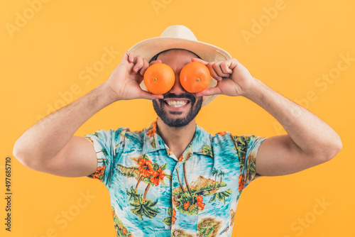 young attractive Latin American man laughing and putting oranges on eyes studio shot medium closeup orange background healthy concept. High quality photo