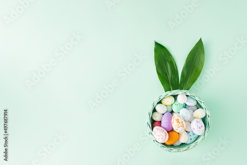 Easter basket with eggs and rabbit ears made of natural leaves on a pastel green background. Minimal holiday flat lay compositin. photo