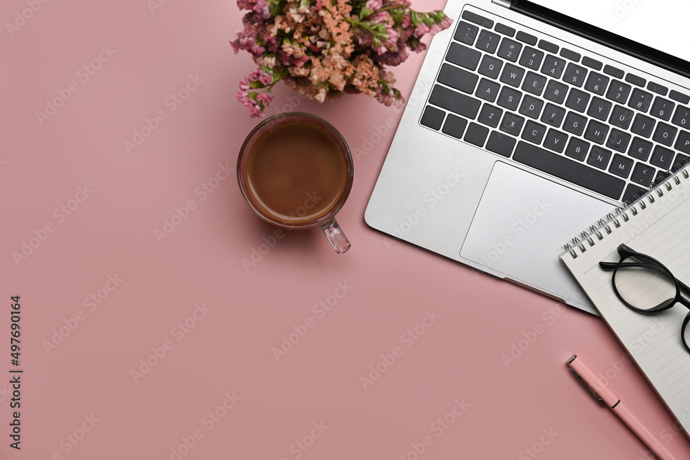 Above view feminine workspace with laptop, notepad, flowers and coffee cup on pink background. Above view feminine workspace with laptop, notepad, flowers and coffee cup on pink background.