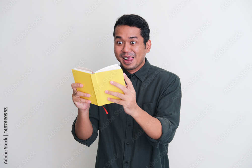Adult Asian man showing funny excited expression while reading a book Adult Asian man showing funny excited expression while reading a book