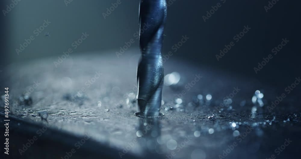 Macro shot of tip of drill machine drilling hole with circular motion with silver metal shavings during steel machining process in heavy industry factory.