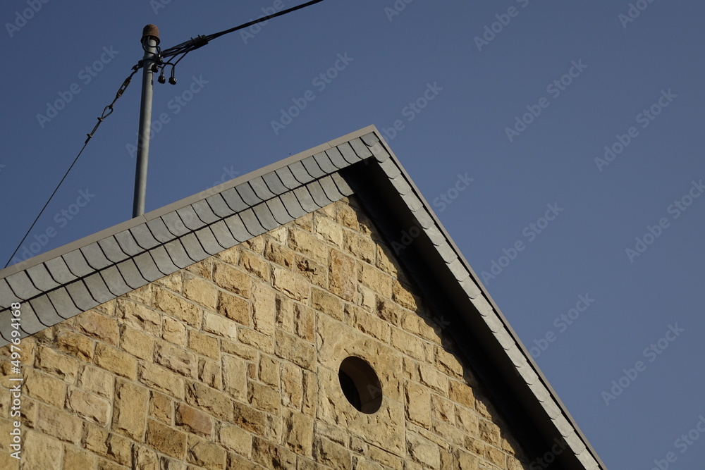 Yellow sand stone gable and black slate shingle roof with power line under a blue Palatinate sky, use: background, copy space (horizontal), Gimmeldingen, RLP, Germany