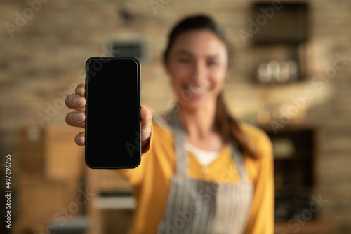 Cinematic shot of smiling female artisan baker is showing in camera smartphone for online commerce applications for checking customer service and selling orders summary of baked goods in bakery shop.