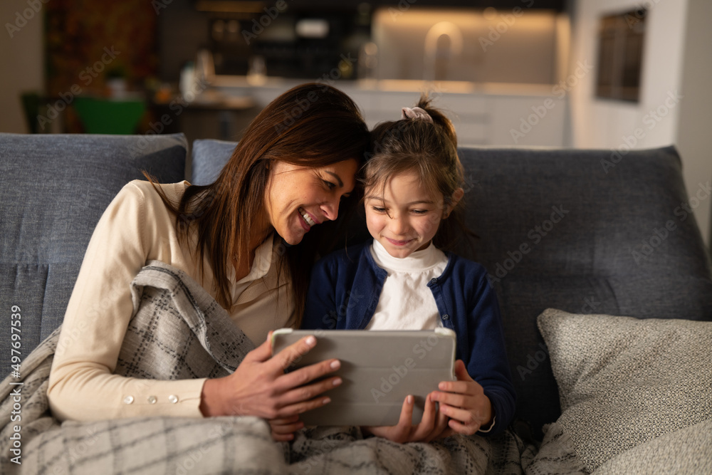 Cinematic shot of happy smiling mother and her cute little girl daughter using technology digital tablet together for family entertainment in living room at home. Cinematic shot of happy smiling mother and her cute little girl daughter using technology digital tablet together for family entertainment in living room at home.