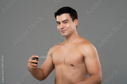Shirtless handsome man using deodorant body spray in light gray isolated studio background