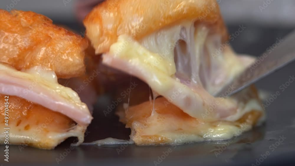 Knife cuts hot baked sandwich with cheese and ham on plate. French toast with melted cheese for breakfast. Food background close-up Knife cuts hot baked sandwich with cheese and ham on plate. French toast with melted cheese for breakfast. Food background close-up