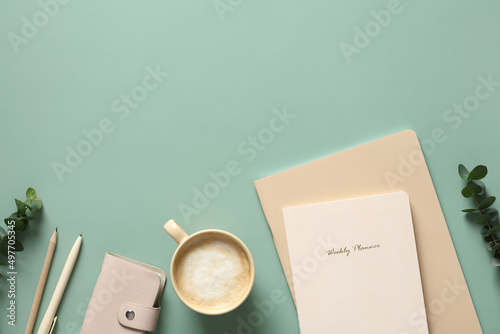Aesthetic minimalist style home office desk table with notebooks, cup of coffee, feminine accessories and eucalyptus leaves on green background. Flat lay, to view.
