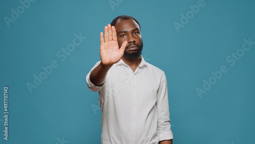 Negative person doing stop symbol with palm in studio, expressing denial and rejection. Young man denying and disapproving with idea, raising hand to dismiss and decline suggestion.