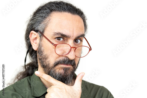 Bearded man with long hair looking over glasses, selective focus. Man pretended to take his hand to his chin.