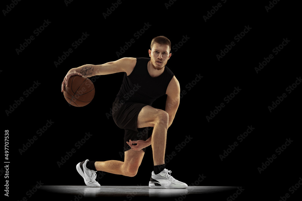 Ground move. Dynamic portrait of young man, basketball player in black uniform training isolated on dark background. Achievements, sport career, motion concepts. Ground move. Dynamic portrait of young man, basketball player in black uniform training isolated on dark background. Achievements, sport career, motion concepts.